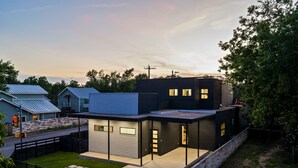 A modern two-story house with a garage, a covered patio, and a stone retaining wall. - Skyline in Hyde ~Two Rooftop Terraces~ Pool+Spa (Austin)