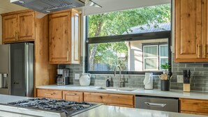 A kitchen with wooden cabinets, a stainless steel refrigerator, a gas stove, a sink, and a window with a view of trees. - Skyline in Hyde ~Two Rooftop Terraces~ Pool+Spa (Austin)
