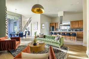Een ruime woonkamer met een groene bank, een ronde salontafel en een trap naar een hoger niveau.