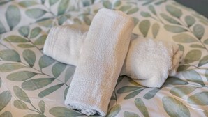 Una cama con una colcha estampada con hojas y dos toallas enrolladas.