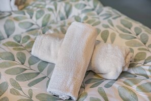Ein Bett mit Bettdecke mit Blattmuster und zwei zusammengerollte Handtücher.