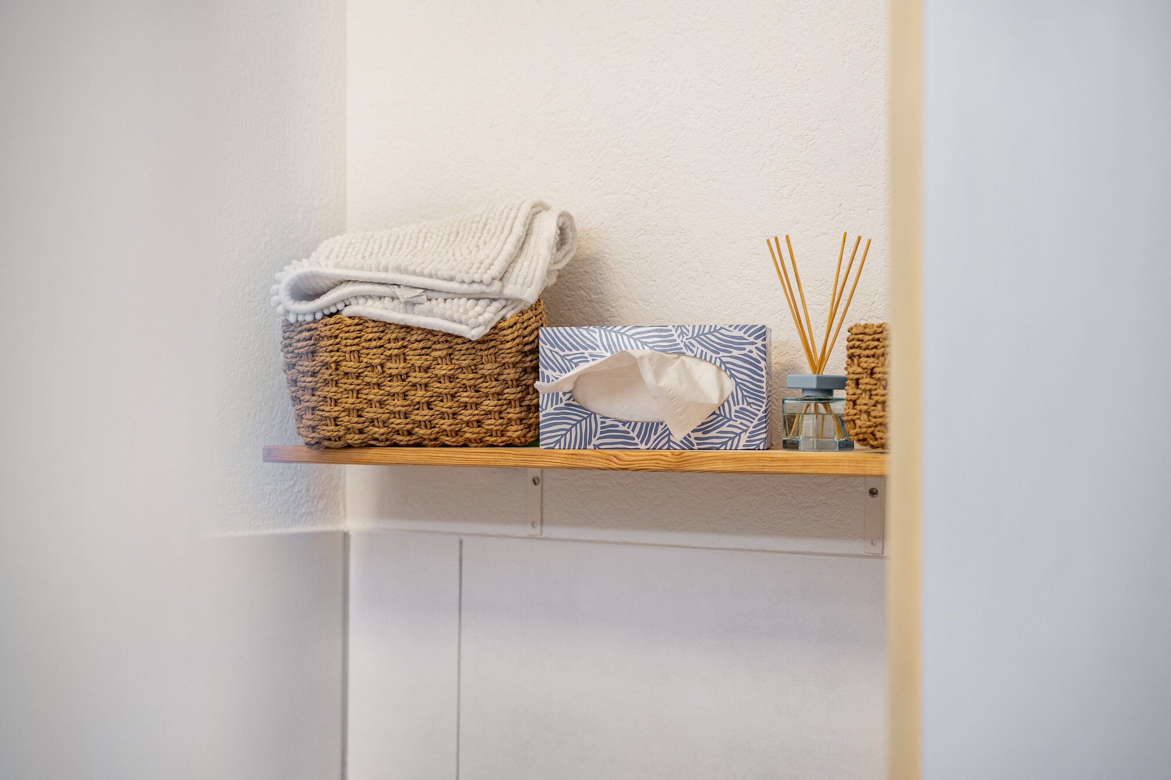 A shelf with a woven basket, a folded towel, a decorative box, and reed diffusers.