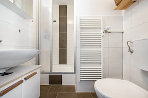 Ein Badezimmer mit einem weißen Waschbecken, einer Dusche, einer Toilette und einem Handtuchhalter.