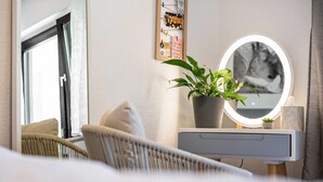 Un dormitorio con cama, mesita de noche con espejo, planta en maceta y un cuadro colgado en la pared.