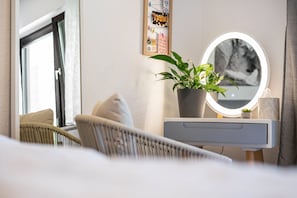 A bedroom with a bed, a bedside table with a mirror, a potted plant, and a wall-mounted picture.
