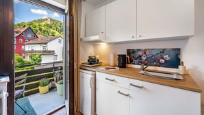 Una cocina moderna con armarios blancos, encimera de madera y vista a una casa roja a través de un ventanal.