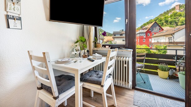 Un comedor con mesa, sillas, televisor y vista a una casa roja a través de una ventana.