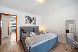 Ein Schlafzimmer mit einem Bett, einem Sessel, einem Nachttisch und einem Wandbild.