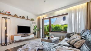 Una sala de estar moderna con televisor de pantalla plana, sofá de cuero y un gran ventanal con vista a follaje.