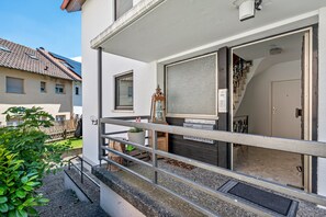 A residential building with a balcony, a wooden door, and a small garden area.