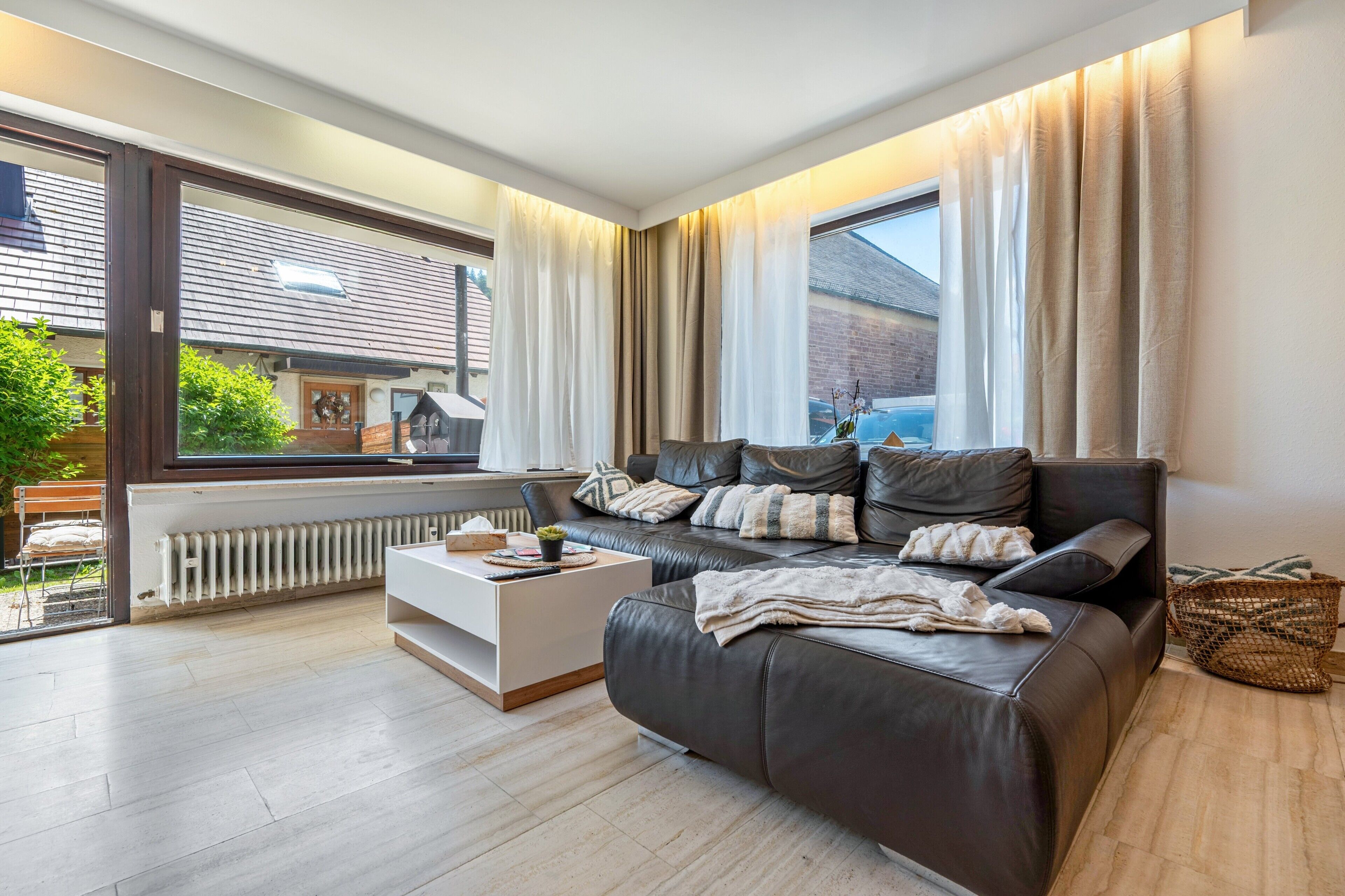 Un salon moderne avec un canapé en cuir, une table basse blanche et une grande fenêtre agrémentée de rideaux.