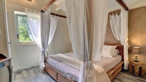 A four-poster canopy bed with a wooden headboard, a bedside table with a lamp, and a window with curtains. - La Béalière - A 4-star haven of peace in the heart of Ardèche (Labeaume)