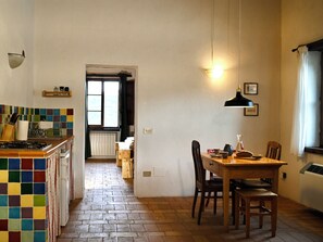 A kitchen with a tiled backsplash, a dining area with a table and chairs, and a window with curtains. - Accessible seclusion: holiday apartment with saltwater pool and wood-fired sauna (Piegaro)