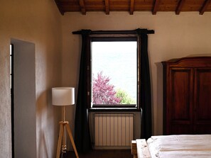 A room with a bed, a radiator, a window with curtains, and a wooden ceiling. - Accessible seclusion: holiday apartment with saltwater pool and wood-fired sauna (Piegaro)