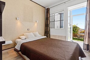 Ein Schlafzimmer mit einem Bett, einem Fenster mit Vorhängen und Blick ins Freie.