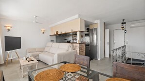 A modern living room with a sofa, a glass dining table with woven placemats, a kitchen area with a refrigerator, and a staircase with metal railings. - 2 Bed Panoramic Sea Views RDR543 (Benalmádena)