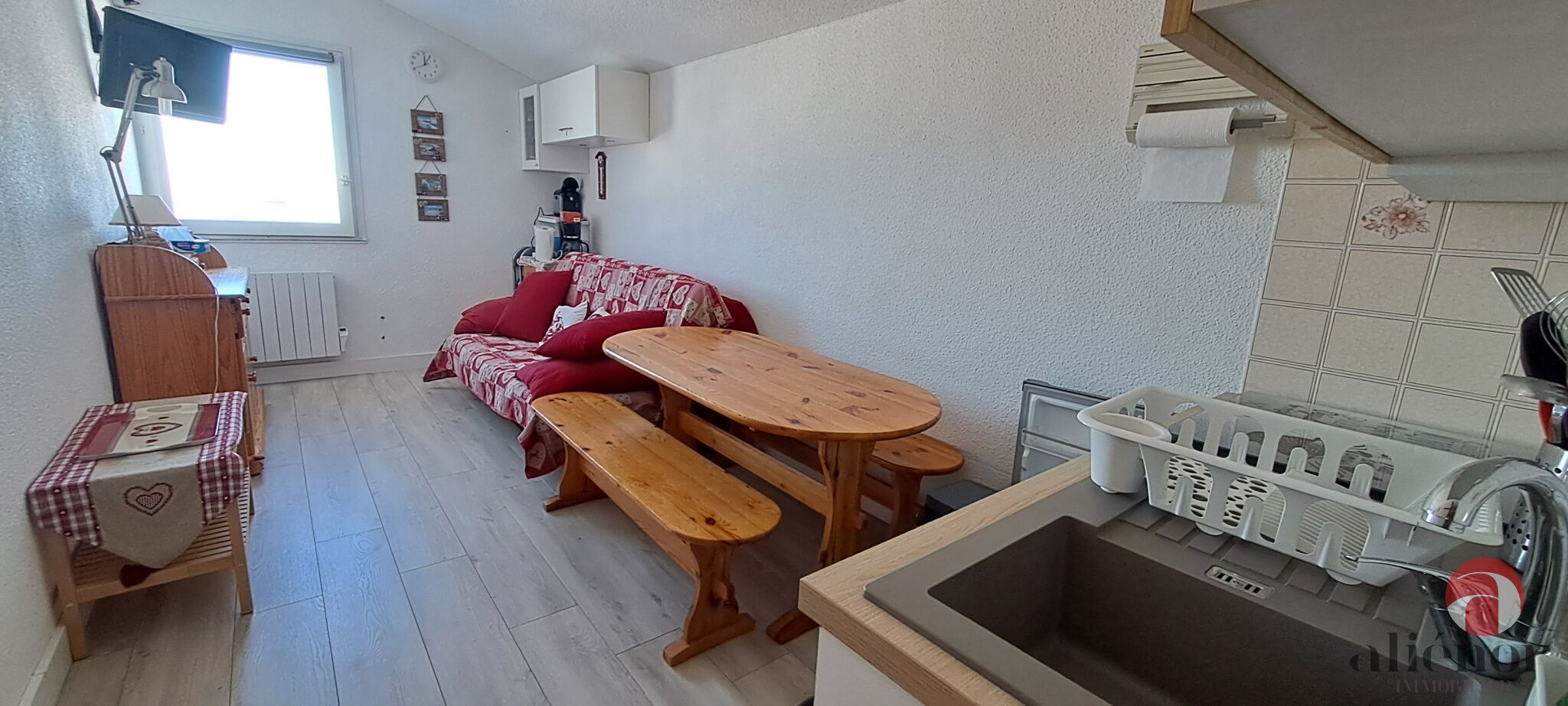 Een kleine keuken met een houten tafel en bankje, een gootsteen en een raam.