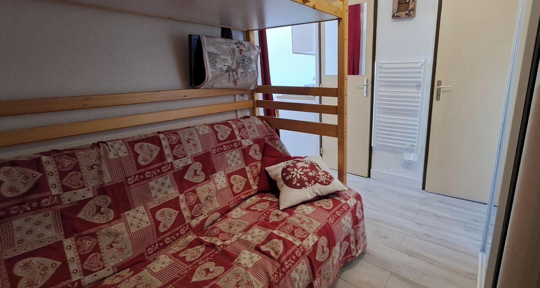 Een kamer met een houten stapelbed, een gestreept sofa, een decoratief kussen, en een schuifdeur.