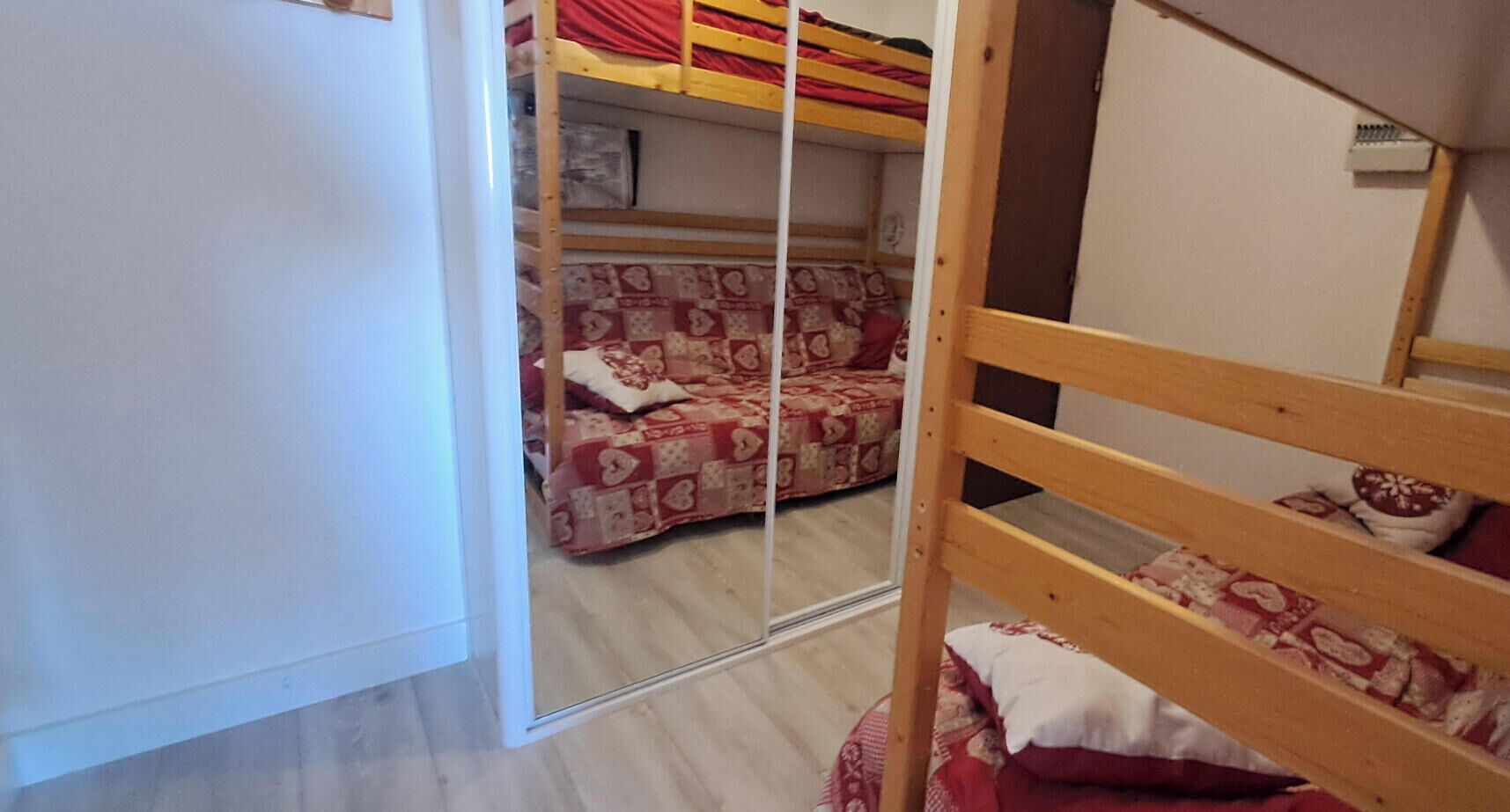 Una habitación con literas, un armario con espejo y una colcha estampada.