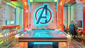 A room with a foosball table, a neon Avengers logo, and a computer monitor on a desk. - 5BR house sleeps 14 near Disney area (Clermont)