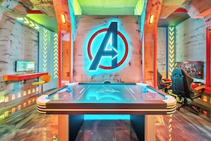 A room with a foosball table, a neon Avengers logo, and a computer monitor on a desk. - 5BR house sleeps 14 near Disney area (Clermont)