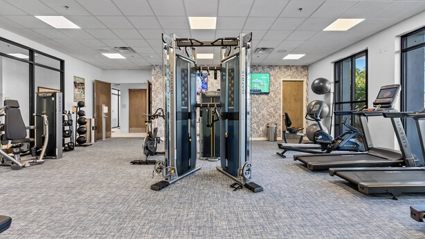 A gym with treadmills, a weight machine, and a wall-mounted TV. - 5BR house sleeps 14 near Disney area (Clermont)
