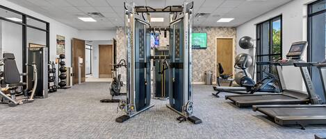 Une salle de sport équipée de tapis de course, d’une machine de musculation et d’un téléviseur fixé au mur.