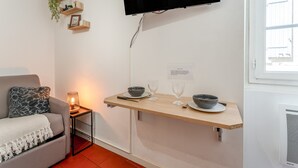 A modern living space with a sofa, a TV mounted on the wall, a wooden shelf with bowls and glasses, and a small table with a lamp. - Holiday Home 'Studio Cocooning Beaucaire C3' with Wi-Fi (Beaucaire)