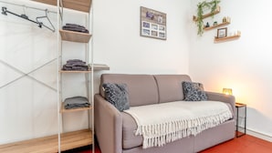 A living room with a sofa, a wooden shelf unit, a wall-mounted coat rack, and a small table with a lamp. - Holiday Home 'Studio Cocooning Beaucaire C3' with Wi-Fi (Beaucaire)
