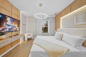 A modern bedroom with a large bed, a TV mounted on the wall, and a window with curtains. - 8BR house with private pool in Solara Resort (Kissimmee)