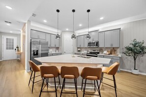 A modern kitchen with a central island, bar stools, stainless steel appliances, and pendant lighting. - 8BR house with private pool in Solara Resort (Kissimmee)