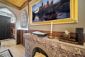 A room with a stone fireplace, a framed painting of a castle, a white candle, and a stack of books. - 8BR house with private pool in Solara Resort (Kissimmee)