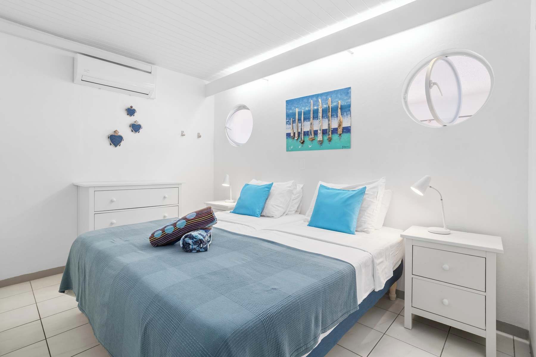 Une chambre à coucher comprenant un lit, des tables de chevet, un climatiseur fixé au mur et un tableau.