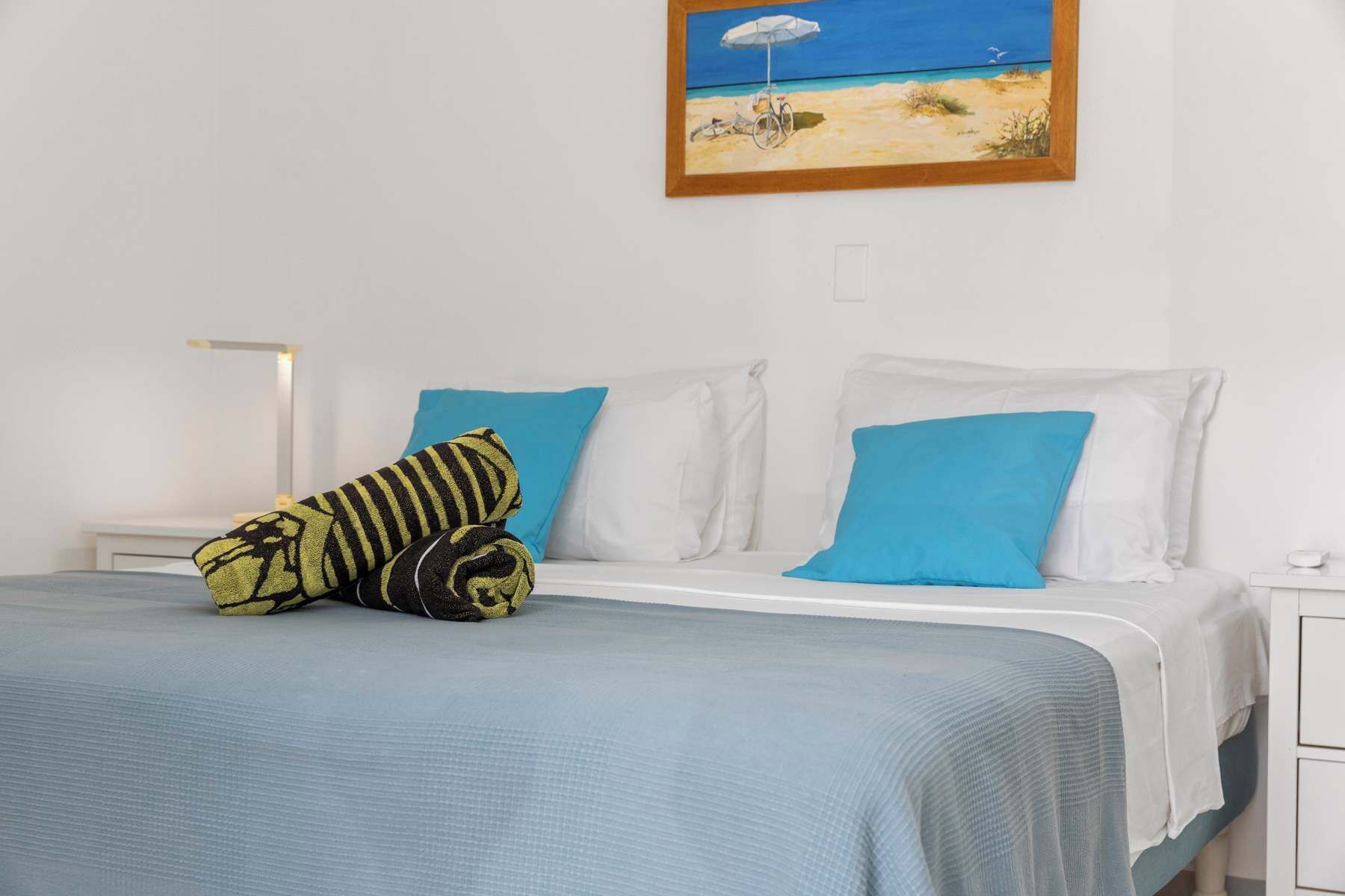 A bed with a blue bedspread, two white pillows, one blue pillow, and a striped pillow.