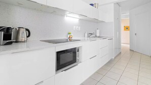 Une cuisine moderne avec des meubles blancs, un four encastré, une bouilloire et un four à micro-ondes.