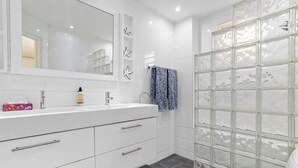 Une salle de bain moderne avec un meuble-lavabo blanc, un grand miroir, une douche en verre et des toilettes.