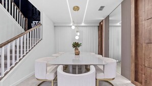 Uma área de refeições moderna com uma mesa branca, cadeiras combinando e uma escada com grades de madeira.