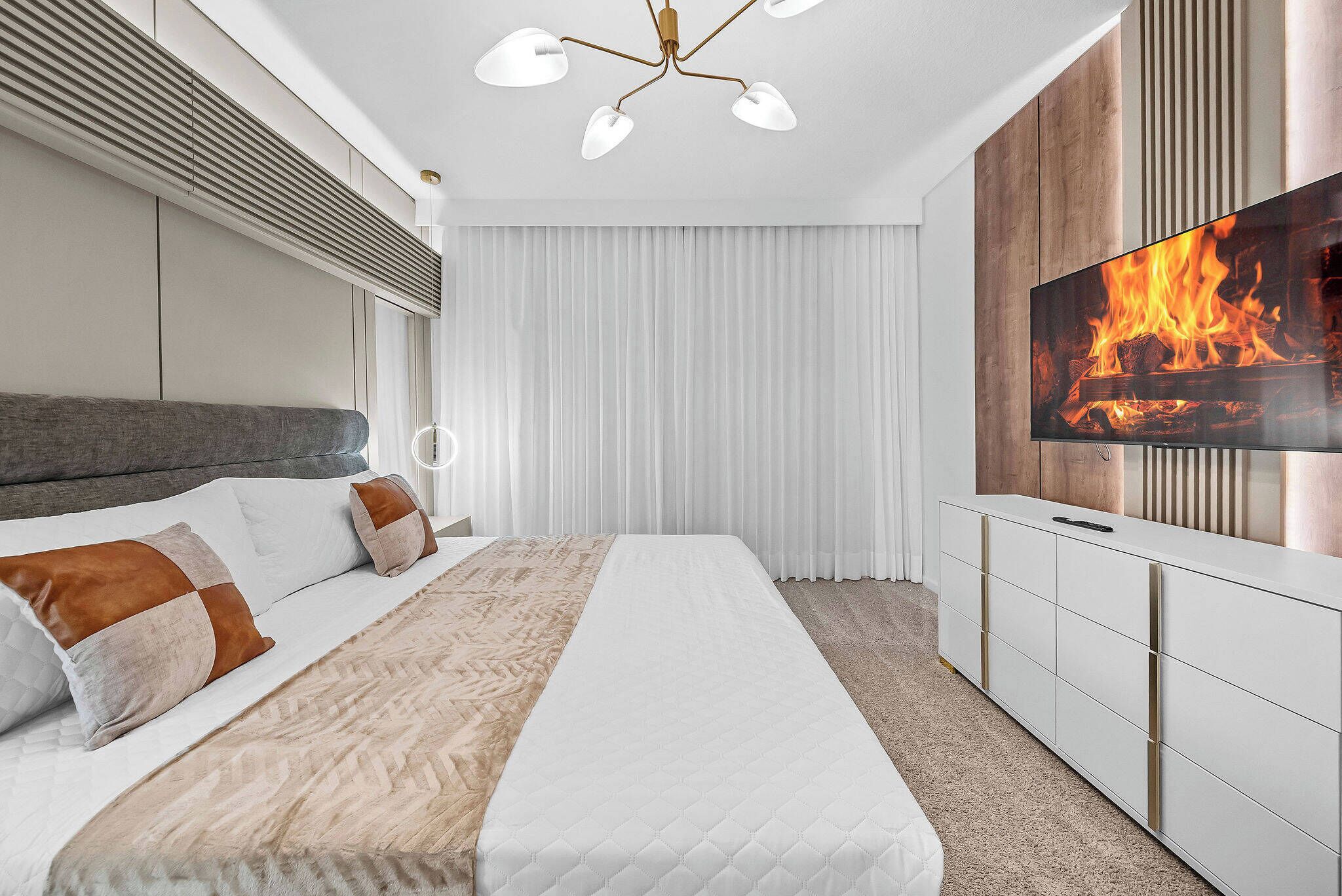 A modern bedroom with a bed, a TV, and a ceiling fan.
