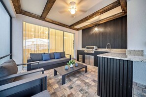A modern outdoor living space with a sofa, coffee table, and a built-in kitchen area. - 8BR house with private pool in Solara Resort (Kissimmee)