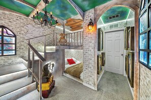 Una habitación con una escalera, una cama con un cojín rojo, una escultura de perro y una araña.