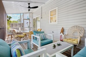 A covered outdoor seating area with wicker furniture, a ceiling fan, and a view of the house.
