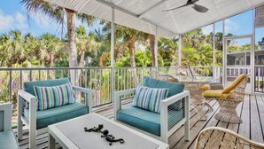 A covered outdoor seating area with white furniture, a ceiling fan, and a view of palm trees. - Palm Breeze - 3 Bedroom Mins from Beach (Holmes Beach)