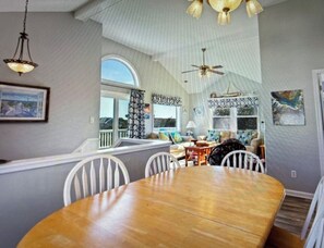 A dining area with a wooden table and chairs, a ceiling fan, and a view of the outdoors. - Ocean Sands 4 Bedroom Private Pool In Culdesac Walk to Beach! The Drift - Woods (COROLLA)