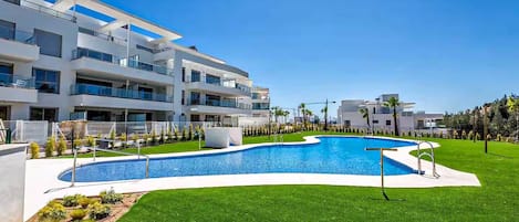 A modern building with a swimming pool, surrounded by well-maintained grass and palm trees.