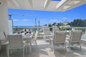 A terrace with a dining table set for two, outdoor chairs, and a view of the sea and buildings. - Luxury Sea, Pool & Mountain View Apt near La Cala (Mijas Costa)