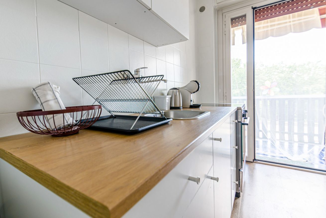 Una cocina con mostrador de madera, un estante metálico, una tetera y un lavamanos.