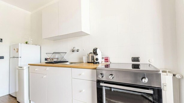 Een kleine keuken met witte kastjes, een roestvrijstalen oven, een koffiezetapparaat en een waterkoker op het aanrecht.