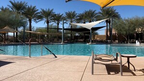 Zona junto a la piscina con un amplio toldo amarillo, palmeras y sillas de descanso.