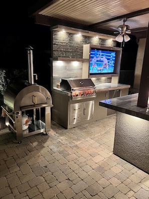 Eine Außenküche mit Grill, Fernseher und Räucherofen.