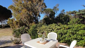 Terassi, jossa on valkoinen pöytä ja tuolit, ja jonka ympärillä on vehreää kasvillisuutta ja puita.